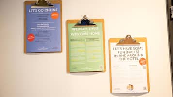 Three informational signs on a wall: 'LET'S GO ONLINE' with WiFi details, 'WELCOME THUIS' with hotel information, and 'LET'S HAVE SOME FUN (FACTS) IN AND AROUND THE HOTEL' with fun facts.