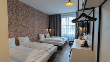 Habitación de hotel con pared de ladrillo, dos camas, un escritorio y una planta colgante.