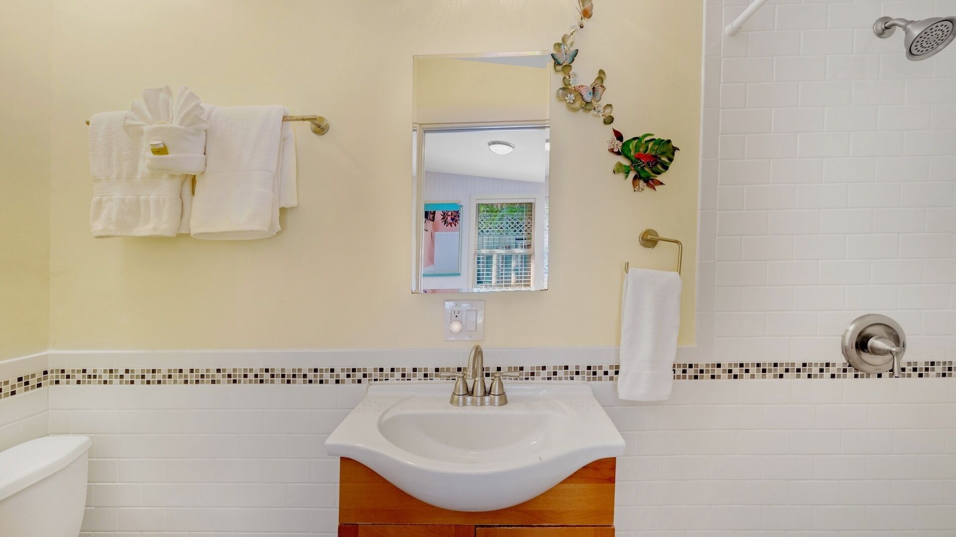 A bathroom with a white sink, a mirror, and a shower. There are towels hanging on a rack and a decorative plant on the wall.