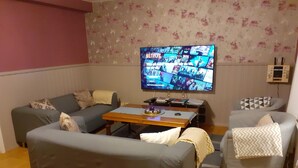 Un salon doté d’un téléviseur à écran plat affichant l’interface de Netflix, d’une table basse en bois et de deux canapés gris ornés de coussins à motifs.