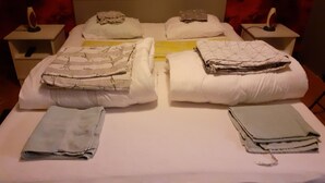 Un lit bien fait, agrémenté de plusieurs oreillers et de couvertures pliées, deux tables de chevet avec des lampes, et un mur décoré d’un motif rouge.