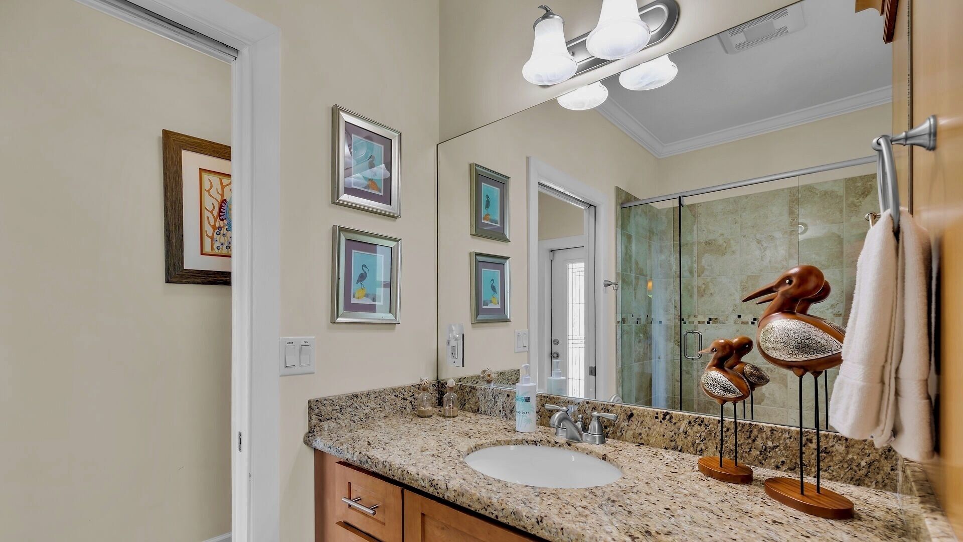 A bathroom with a granite countertop, a sink, a mirror, and framed artwork on the wall.