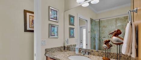 A bathroom with a granite countertop, a sink, a mirror, and framed artwork on the wall.