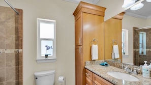 Une salle de bain comprenant des toilettes, un lavabo, un meuble-lavabo, un placard en bois et une fenêtre avec une plante.