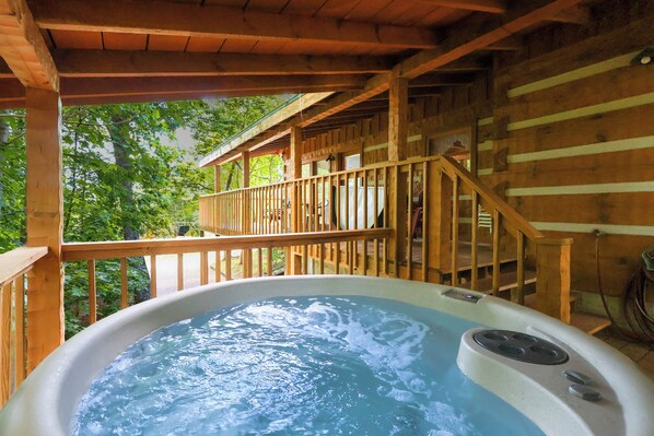 Un jacuzzi en una cabaña de madera con una terraza de madera y una escalera que lleva a un nivel superior.