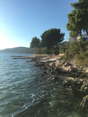 A coastal scene with rocky terrain, clear blue water, and a building with a stone pathway leading to it. - Villa FIG, Cosy Semidetached House@Vranjica-Trogir, Beach40m (Seget Vranjica)