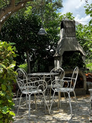 An outdoor patio with a stone fireplace, metal chairs, and a hanging light fixture. - Villa FIG, Cosy Semidetached House@Vranjica-Trogir, Beach40m (Seget Vranjica)