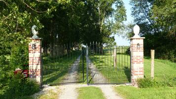A gated entrance with a brick pillar, a metal gate, and a pathway leading into a green area.