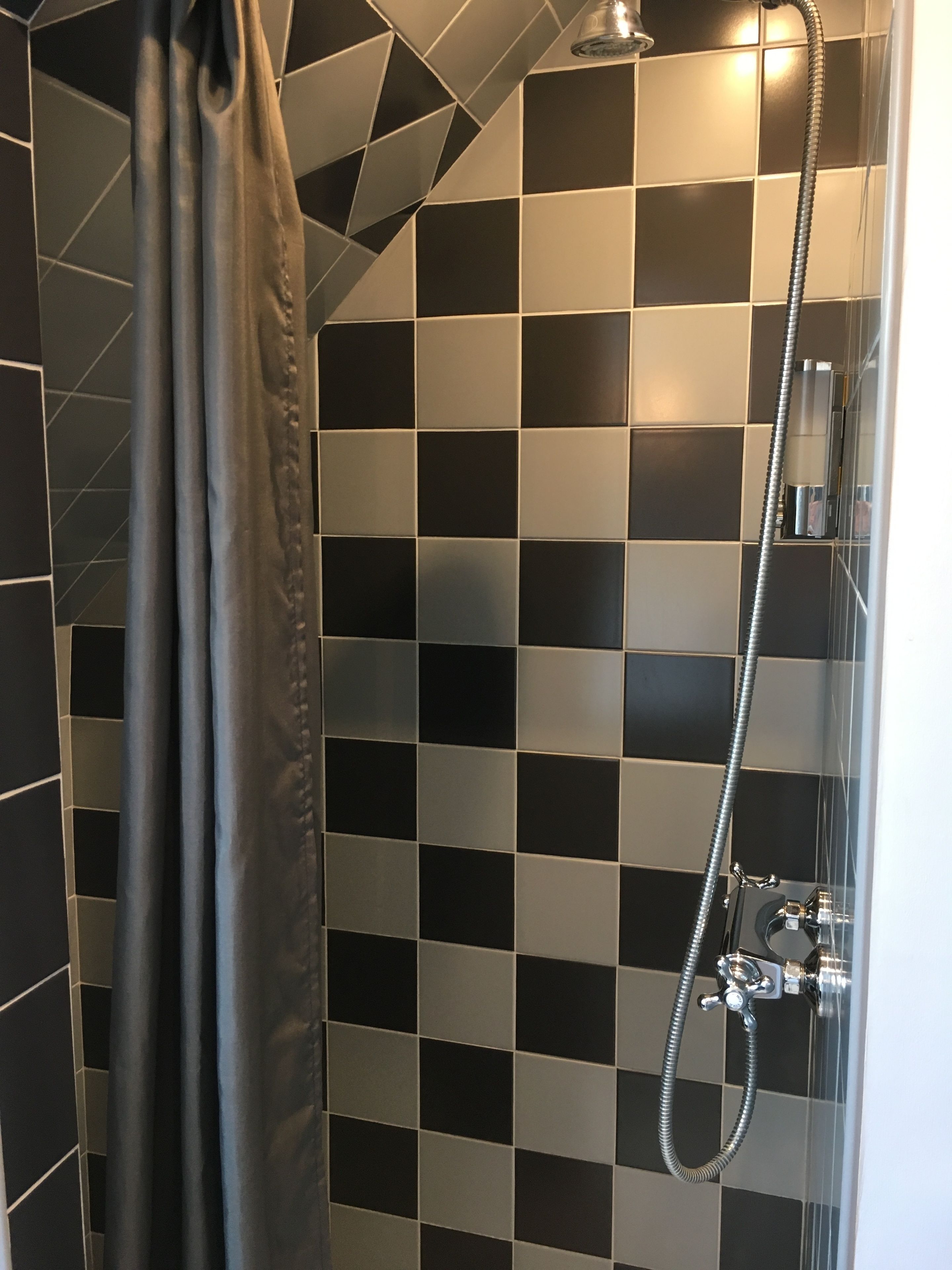 A shower with a checkered black and white tile wall, a showerhead, and a curtain.