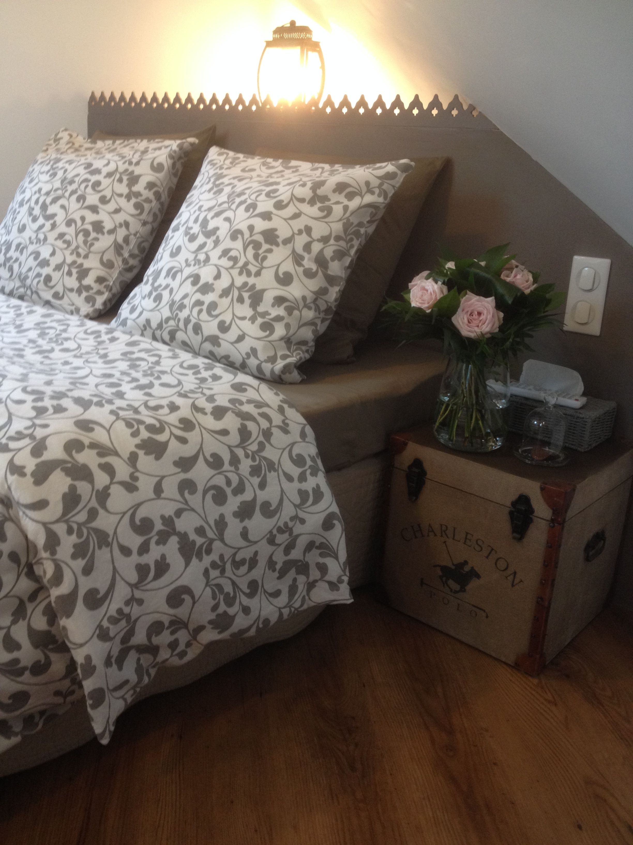 Una cama con ropa de cama estampada, una mesita de noche con un florero y una caja con la etiqueta "Charleston".