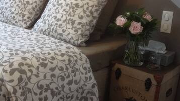 Una cama con ropa de cama estampada, una mesita de noche con un florero y una caja con la etiqueta "Charleston".