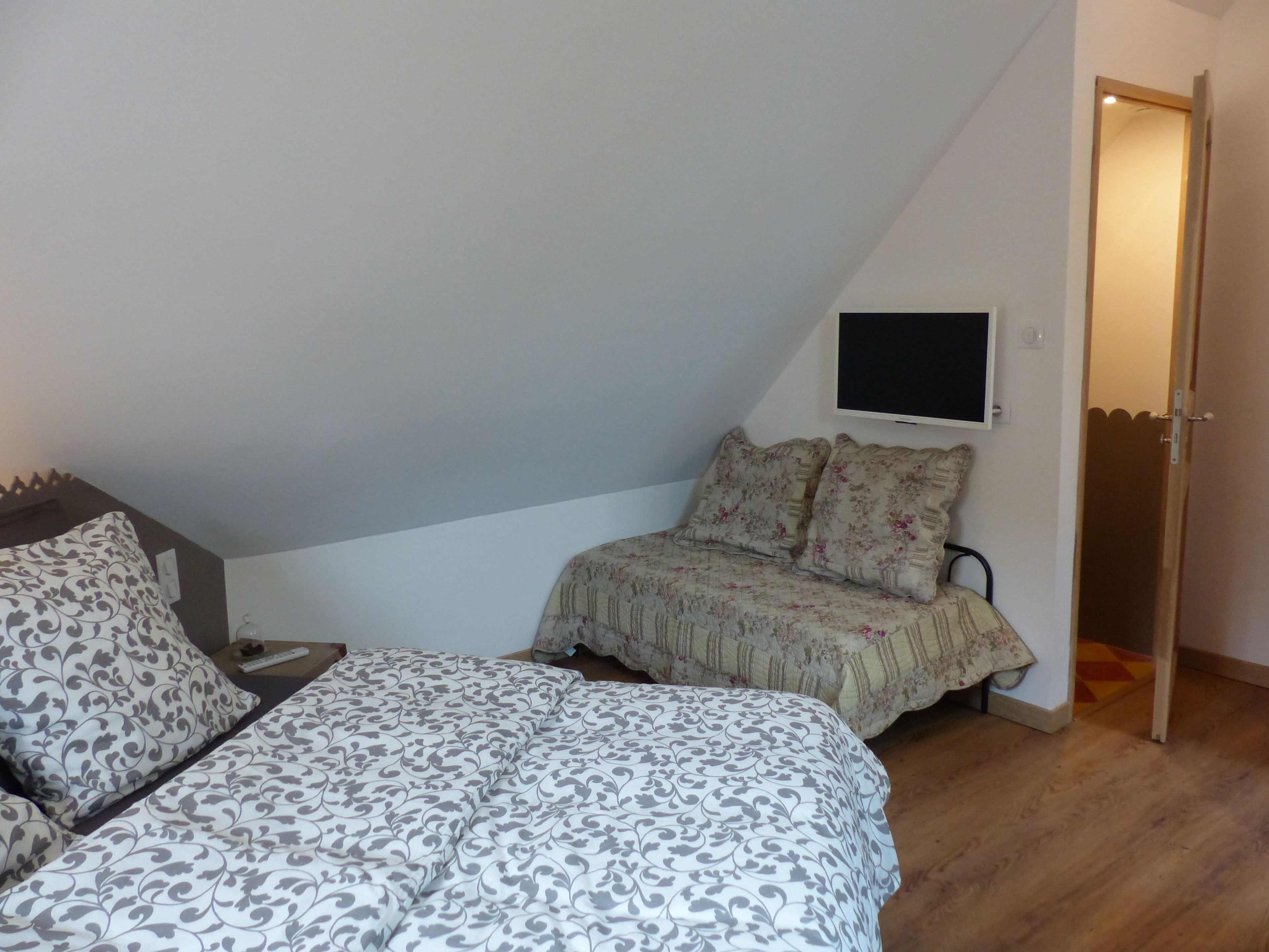 Une chambre à coucher avec un lit, un téléviseur fixé au mur et une porte donnant sur une autre pièce.
