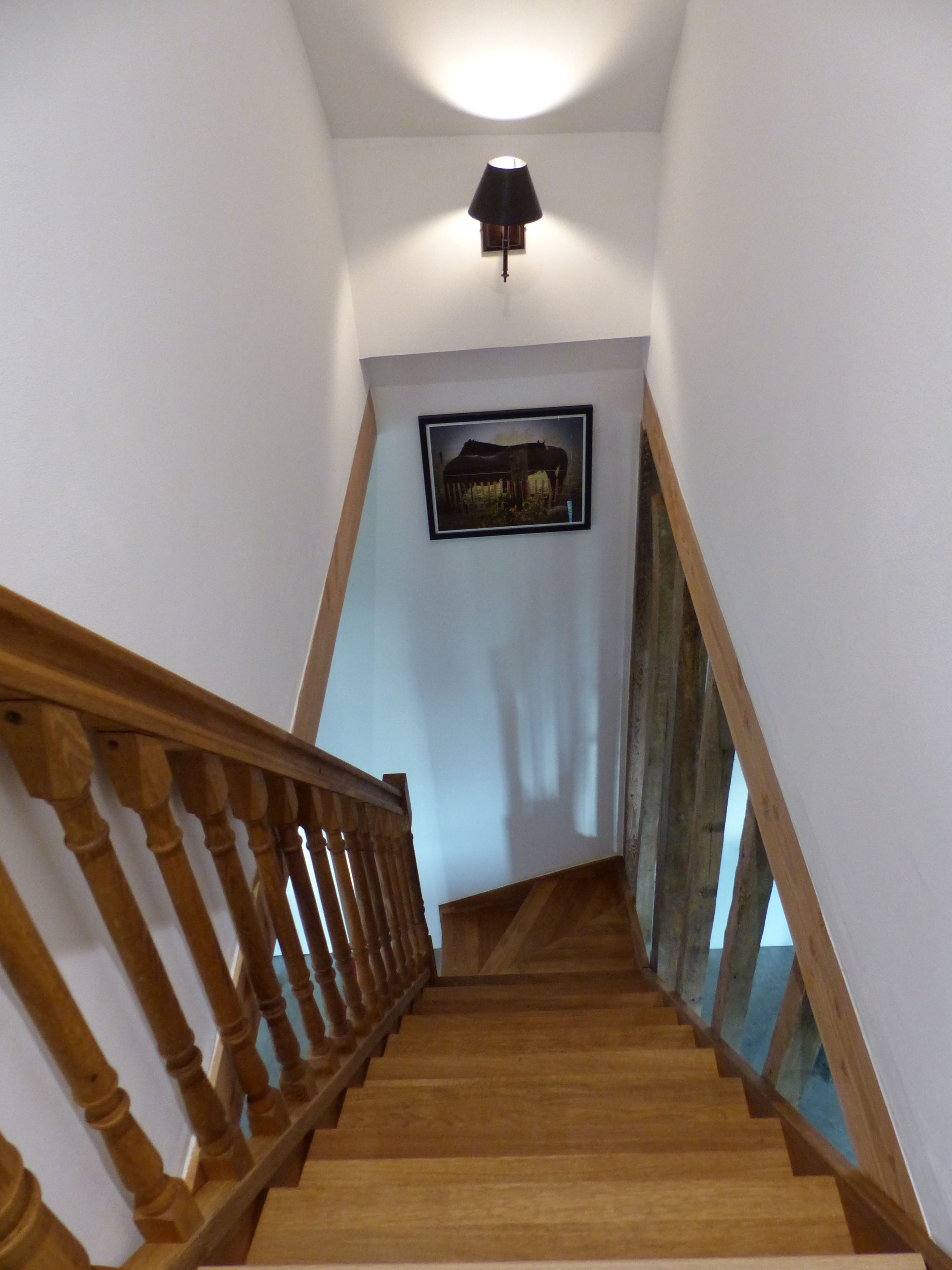 A wooden staircase with a handrail, a framed picture on the wall, and a ceiling light fixture.