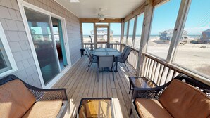 A covered outdoor deck with a table and chairs, a sliding glass door, and a view of the beach and ocean. - The Weathervane | 3BR Carova Beach 4x4 OBX | 4 night stay available | Pets (Carova)