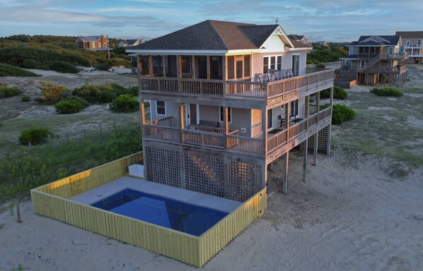 Una casa sulla spiaggia a più piani con piscina, terrazza e diversi balconi.