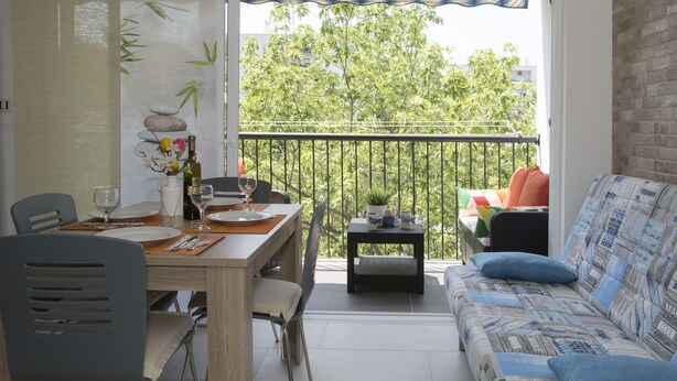 Un balcon comprenant un coin repas, un canapé et une petite table agrémentée d’une plante.