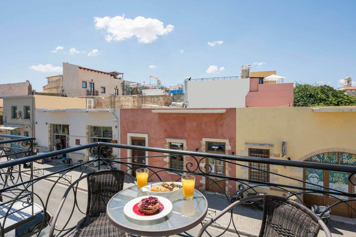 A rooftop terrace with a table set for two, featuring a plate of food and a glass of orange juice.