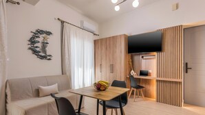 A modern living space with a sofa, dining table, chairs, a TV, and a wooden cabinet. - Porto Orion Studios (Chania)