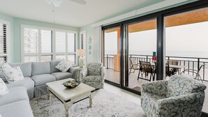 Une pièce comprenant un canapé, des fauteuils, une table basse et donnant sur un balcon aménagé avec des sièges d’extérieur.