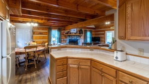 A wooden cabin interior with a kitchen, dining area, and a fireplace.