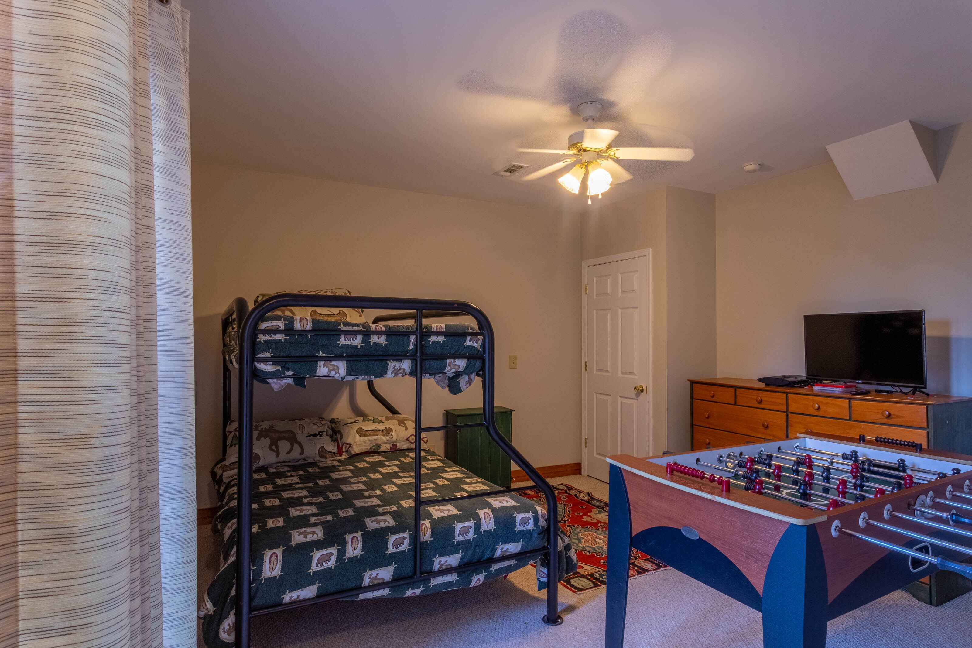 A bedroom with a bunk bed, a ceiling fan, a television, and a foosball table.