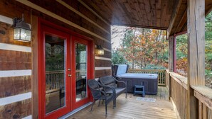 A wooden deck with a red door, wicker chairs, and a hot tub.