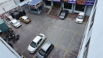Ein Parkplatz mit mehreren Autos und Motorrädern, eine Treppe zu einem Gebäude mit Schildern für eine Bar und ein Restaurant, sowie ein Hotel.