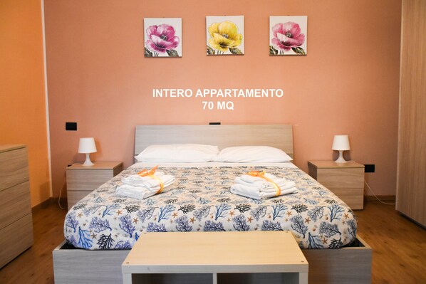 A bedroom with a bed, two bedside tables, and three wall-mounted flower paintings.