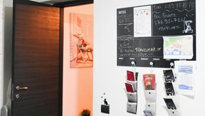 Eine Hotelhalle mit einer dunklen Holztür, einer Wandtafel mit Notizen und einer Karte sowie mehreren Broschüren.