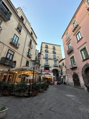 A narrow street with buildings on either side, featuring balconies and outdoor seating areas.