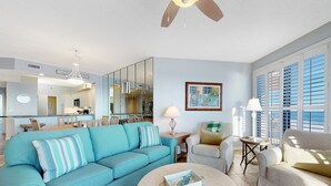 A living room with a blue sofa, a round coffee table, and a view of the kitchen and dining area. - Stunning Gulf Front Views! Sensational Amenities! (Orange Beach)