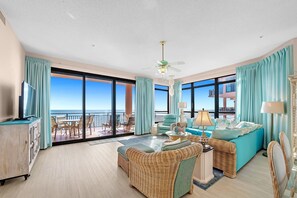 A spacious living room with a large window, a ceiling fan, and a view of the ocean. - Leave Your Footprints in the sand in this Gulf Front condo! (Orange Beach)