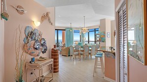 Un vaste espace de vie avec vue sur l’océan, un coin repas avec des meubles en osier, et un mur décoré de coquillages et de plumes.