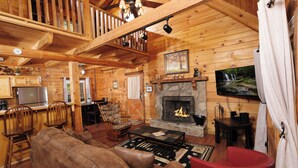 A cozy cabin interior with a fireplace, wooden furniture, and a stone fireplace surround. - Pet friendly 2 bedroom with hot tub, Smoky Mountain view, and arcade game! (Sevierville)