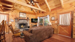 A cozy log cabin interior with a fireplace, wooden furniture, and a television. - Pet friendly 2 bedroom with hot tub, Smoky Mountain view, and arcade game! (Sevierville)