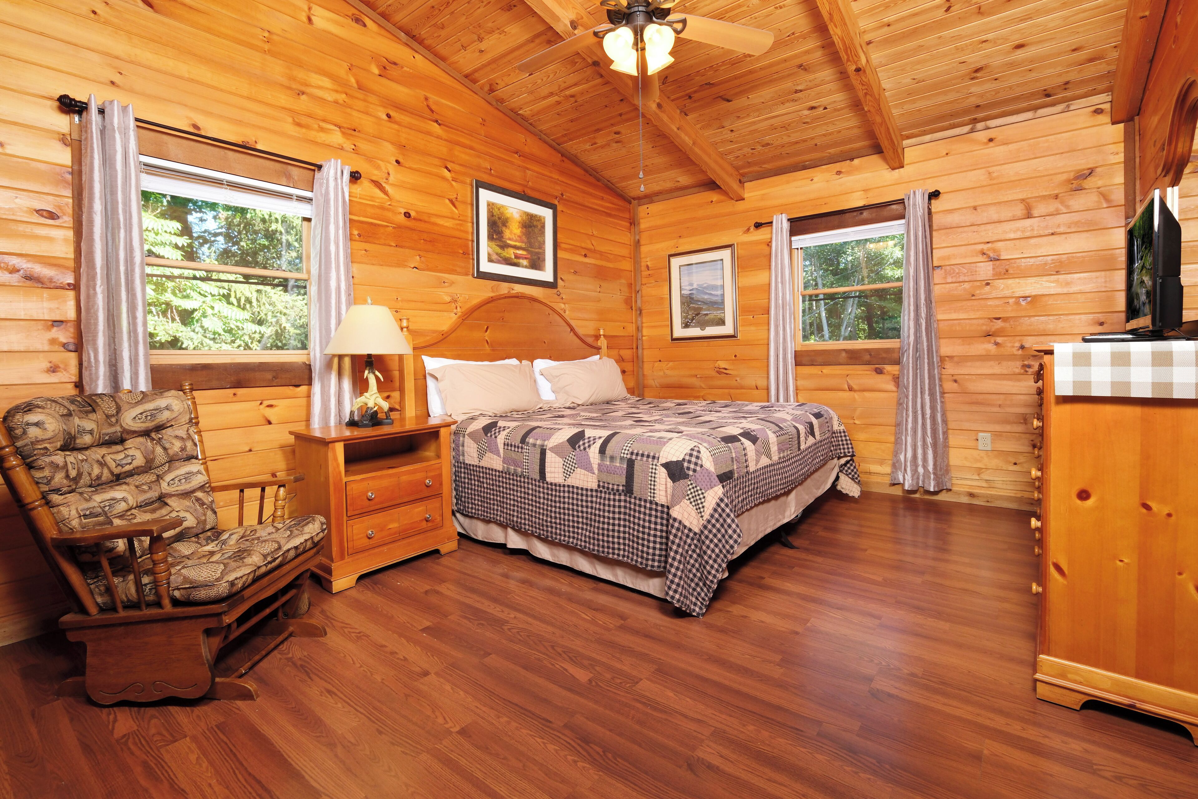 Ein Schlafzimmer einer Holzhütte mit Bett, Stuhl, Nachttisch und Kommode.