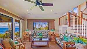 A spacious living room with a view of the ocean, a ceiling fan, and a staircase with wooden railings. - Spectacular Maui Family vacation home - 4 bedroom + den, 4 bath, AC, pool. (Lahaina)