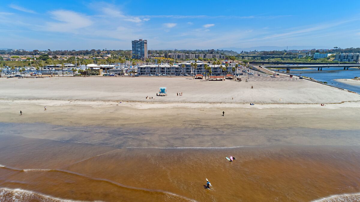 A beach with a lifeguard tower, a parking lot, and a bridge in the background.