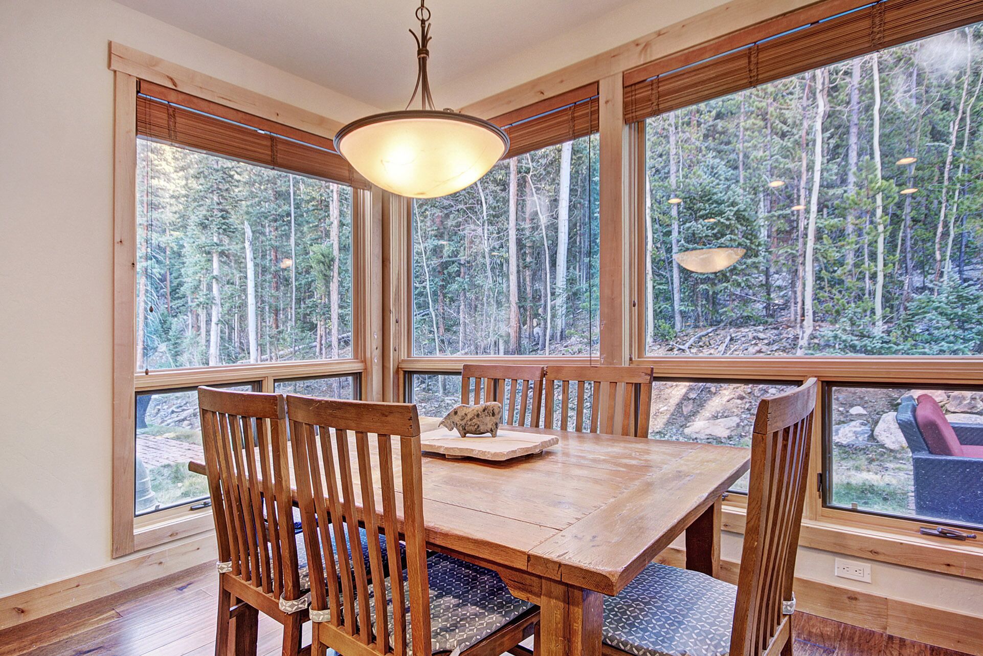 A wooden dining table with chairs, large windows, and a hanging light fixture.