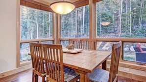 Een houten eettafel met stoelen, grote ramen en een hanglamp.