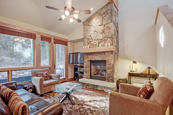 A spacious living room with a stone fireplace, leather sofas, a glass coffee table, and a ceiling fan.