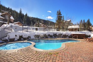 A swimming pool with a brick deck, surrounded by a metal fence and snow-covered ground.