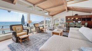 A spacious living area with a high ceiling, large windows overlooking the ocean, wicker furniture, and a wooden dining set. - Stunning, Ocean-Front Home in Seaclift Estates in Cambria! Perfection! (Cambria)