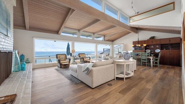 A spacious living area with a high ceiling, large windows overlooking the sea, a cozy seating area, and a wooden dining table. - Stunning, Ocean-Front Home in Seaclift Estates in Cambria! Perfection! (Cambria)