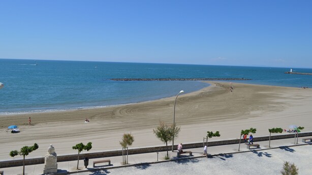 Una playa con cielo despejado, orilla arenosa y algunas personas.