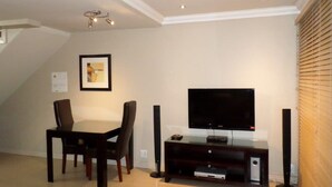 Una sala de estar con una mesa de comedor, sillas, un televisor de pantalla plana y un mueble de madera para equipo electrónico.