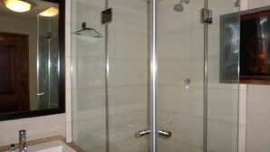 Un baño con ducha de vidrio, lavabo con espejo y puerta de madera.