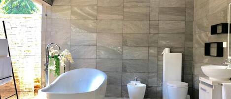 A modern bathroom with a freestanding bathtub, a pedestal sink, and a toilet.