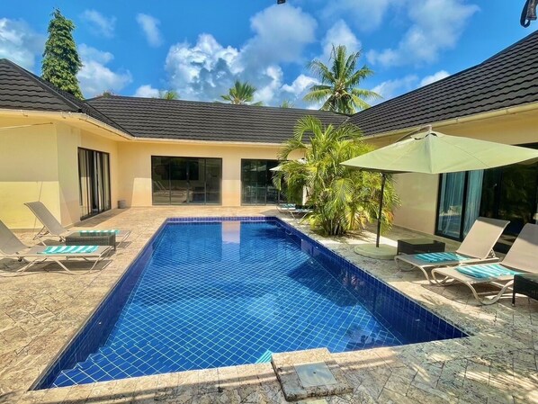 A rectangular swimming pool with blue tiles, surrounded by lounge chairs and a palm tree. - Grand Amber Villas Diani (Diani Beach)