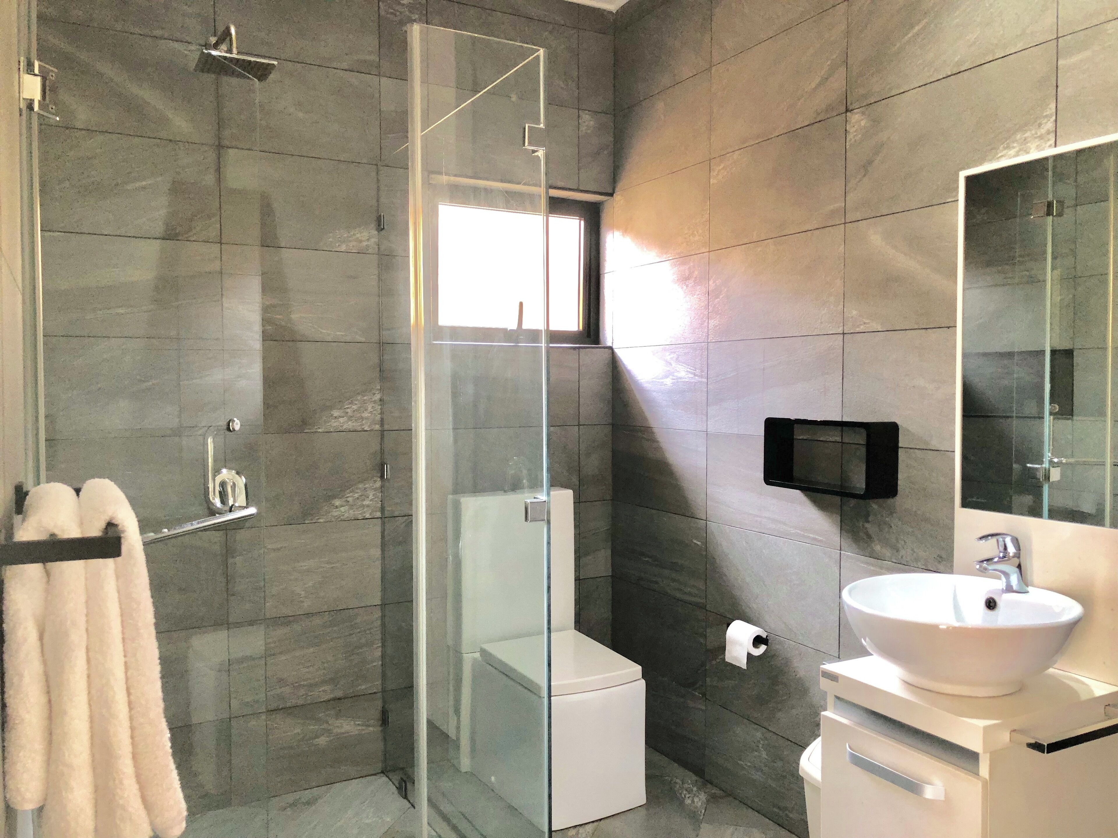 Un baño moderno con ducha envuelta en vidrio, inodoro, lavamanos y un espejo grande.